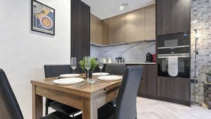 Ein moderner Essbereich mit einem Holztisch, gedeckt für vier Personen, eine Küche mit dunklen Schränken und einer Marmor-Spritzschutzwand sowie eine Wand mit Backsteinverkleidung.