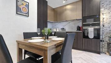 Un'area pranzo moderna con un tavolo in legno apparecchiato per quattro, una cucina con mobili scuri e una parete di mosaico in marmo, e un muro a mattoni a contrasto.