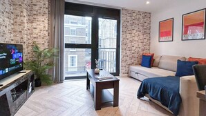 Ein modernes Wohnzimmer mit Fernseher, Sofa und einem großen Fenster.