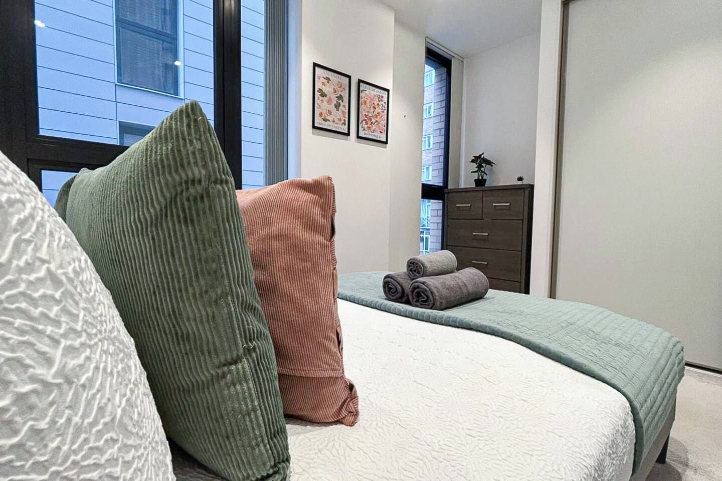 A bedroom with a bed, pillows, a dresser, and a window.