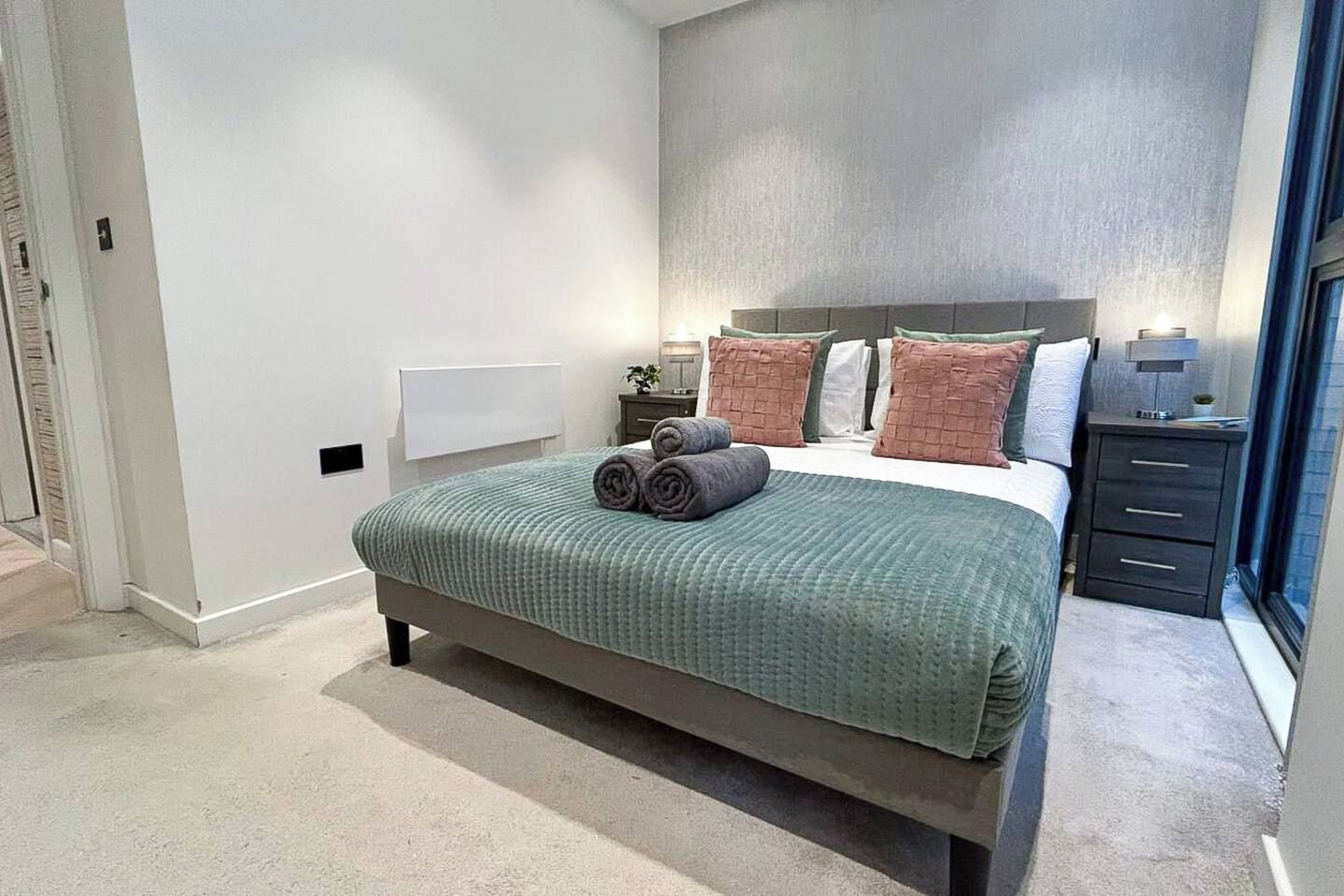 Un dormitorio con cama, almohadas, una mesita de noche y un tocador.