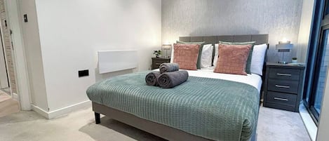 Un dormitorio con cama, almohadas, una mesita de noche y un tocador.