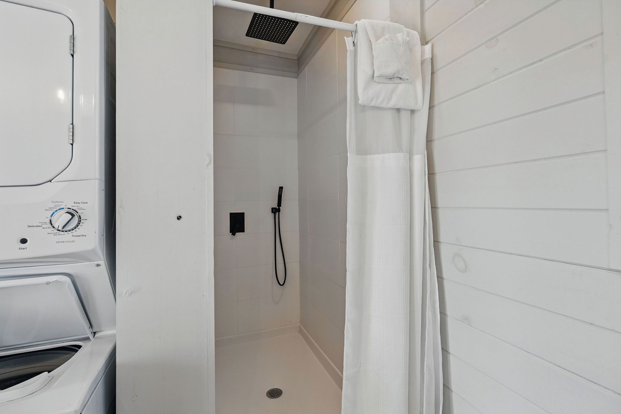 Een badkamer met een douche, een witte handdoek en een zichtbaar bedieningspaneel van een wasmachine.