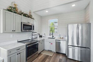 Una cucina moderna con mobili bianchi, elettrodomestici in acciaio inossidabile e una finestra che lascia entrare luce naturale.