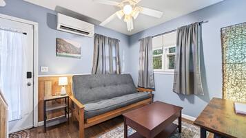 A room with a sofa, a table, a lamp, an air conditioning unit, and a ceiling fan.