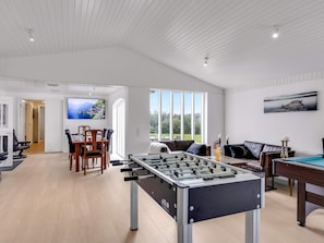 A spacious room with a foosball table, a dining area with chairs and a table, and a large window providing a view of the outdoors. - 4 Star Holiday Home in Lokken (Lokken)