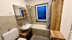 A bathroom with a toilet, sink, shower, and a window with frosted glass.