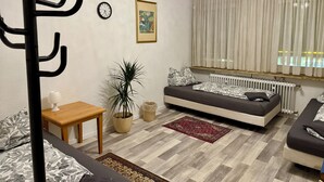 A modern living room with a sofa, a dining table, a potted plant, a clock, and a window with curtains.