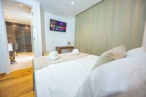 Ein Hotelzimmer mit Bett, einem an der Wand befestigten Fernseher und einem durch eine offene Tür einsehbaren Badezimmer.