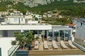A modern building with a rooftop lounge area, glass walls, and a view of a hillside. - Exclusive Penthouse Sara with 3 Bedrooms, Sea View, Hot Tub & Modern Luxury (Makarska)