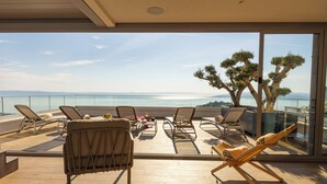 Un balcón con sillones de sol, una mesa con objetos y vistas al mar y a las montañas.