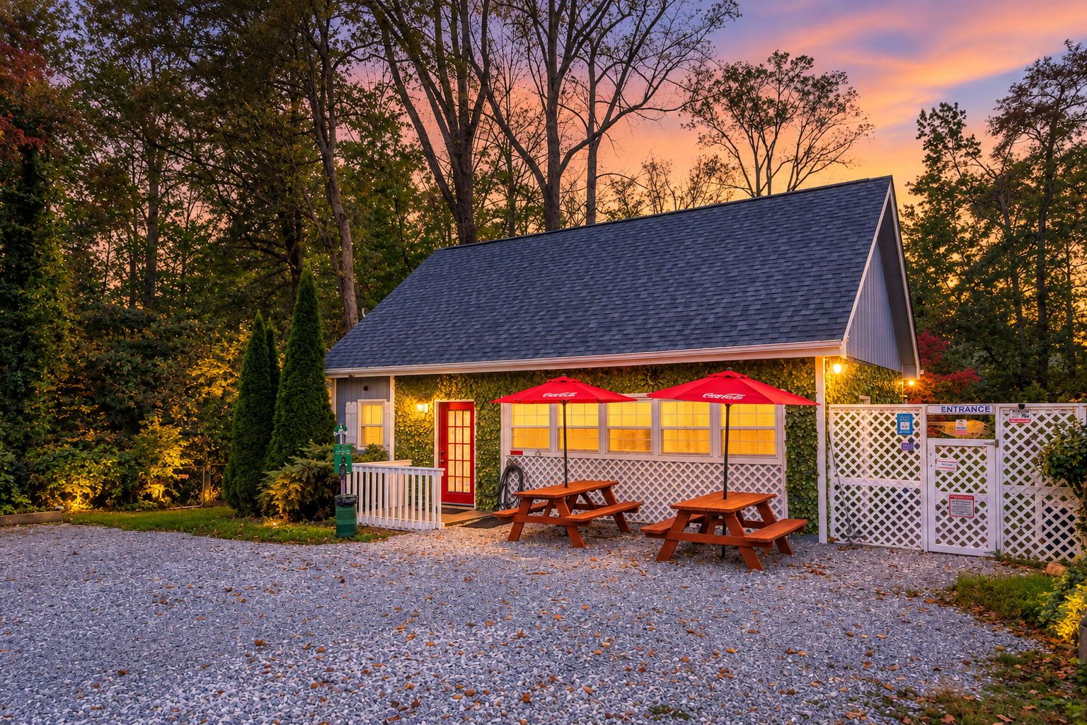 A small building with a red door, two picnic tables, and red umbrellas.