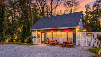 A small building with a red door, two picnic tables, and red umbrellas.