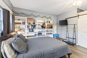Une chambre à coucher avec un grand lit, une armoire, un téléviseur et une étagère contenant divers objets.