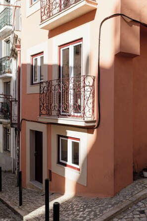 A building with a pink facade, multiple windows, and a decorative iron balcony. - Graça Gate | Mouraria Ground Floor Studio (Lisbon)