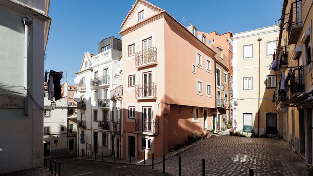 Une rue pavée bordée de bâtiments des deux côtés, dont un bâtiment rose doté de balcons et un bâtiment blanc avec une enseigne.