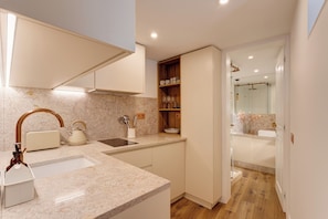 A modern kitchen with a marble countertop, a built-in oven, and a wooden shelf with kitchenware. - Graça Gate | Mouraria Ground Floor Studio (Lisbon)