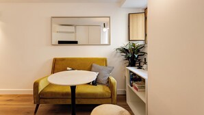 Une pièce avec un fauteuil jaune, une table ronde, un miroir et une bibliothèque contenant des livres et une plante.