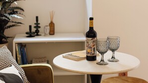 Une pièce avec une table ronde, une bouteille et deux verres. On aperçoit, au fond, une plante, un canapé et un meuble.