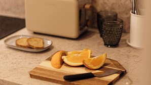 Un comptoir de cuisine avec un grille-pain, une planche à découper avec des tranches d’orange, un couteau et un verre.