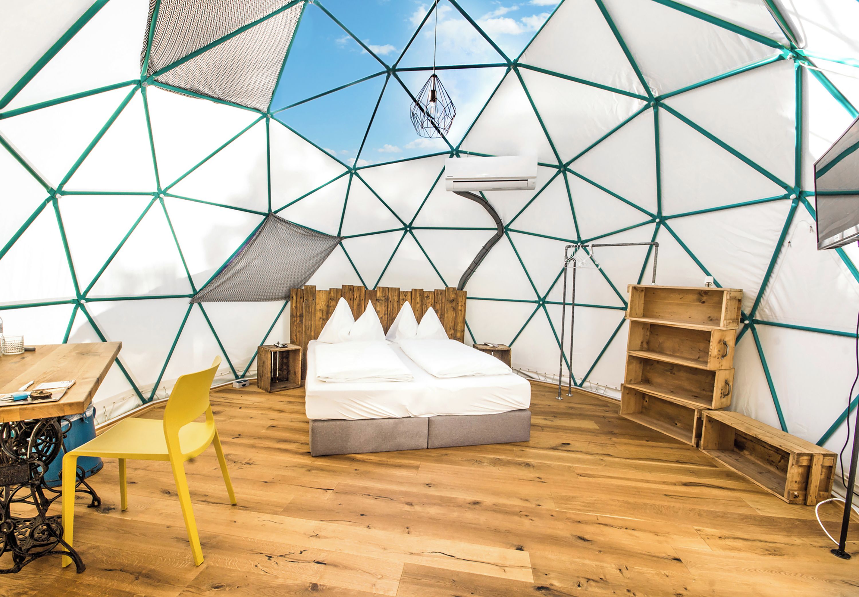 A tented accommodation with a bed, a chair, a table, and a hanging light fixture.