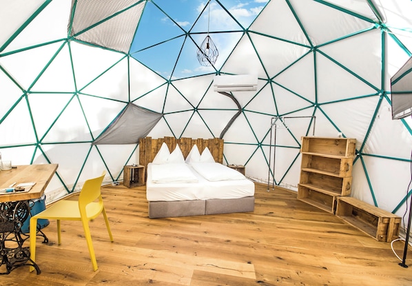 A tented accommodation with a bed, a chair, a table, and a hanging light fixture.