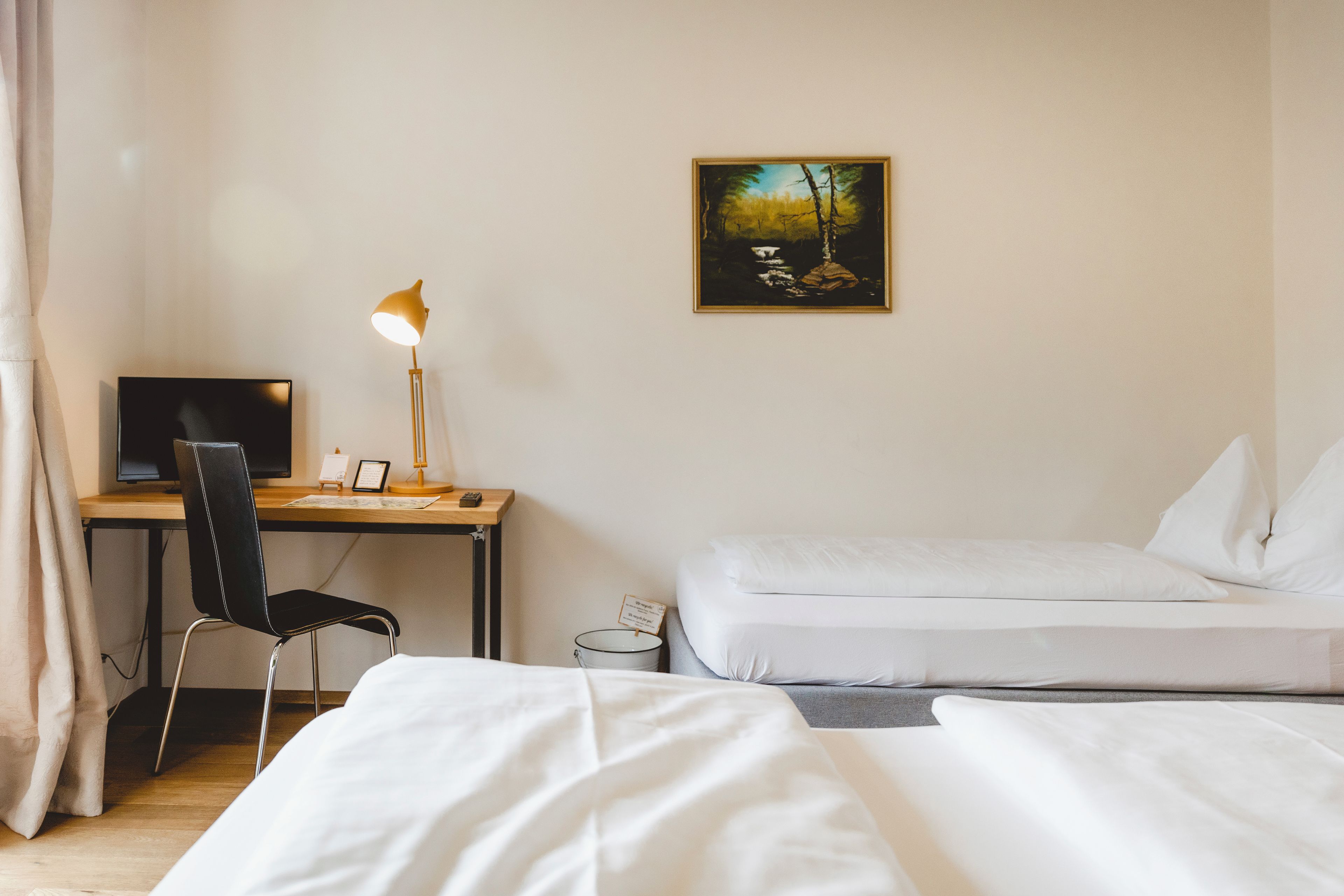 A hotel room with a desk, chair, computer, lamp, and two beds.
