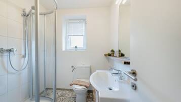 Ein Badezimmer mit Dusche, Toilette, Waschbecken und einem kleinen Fenster.