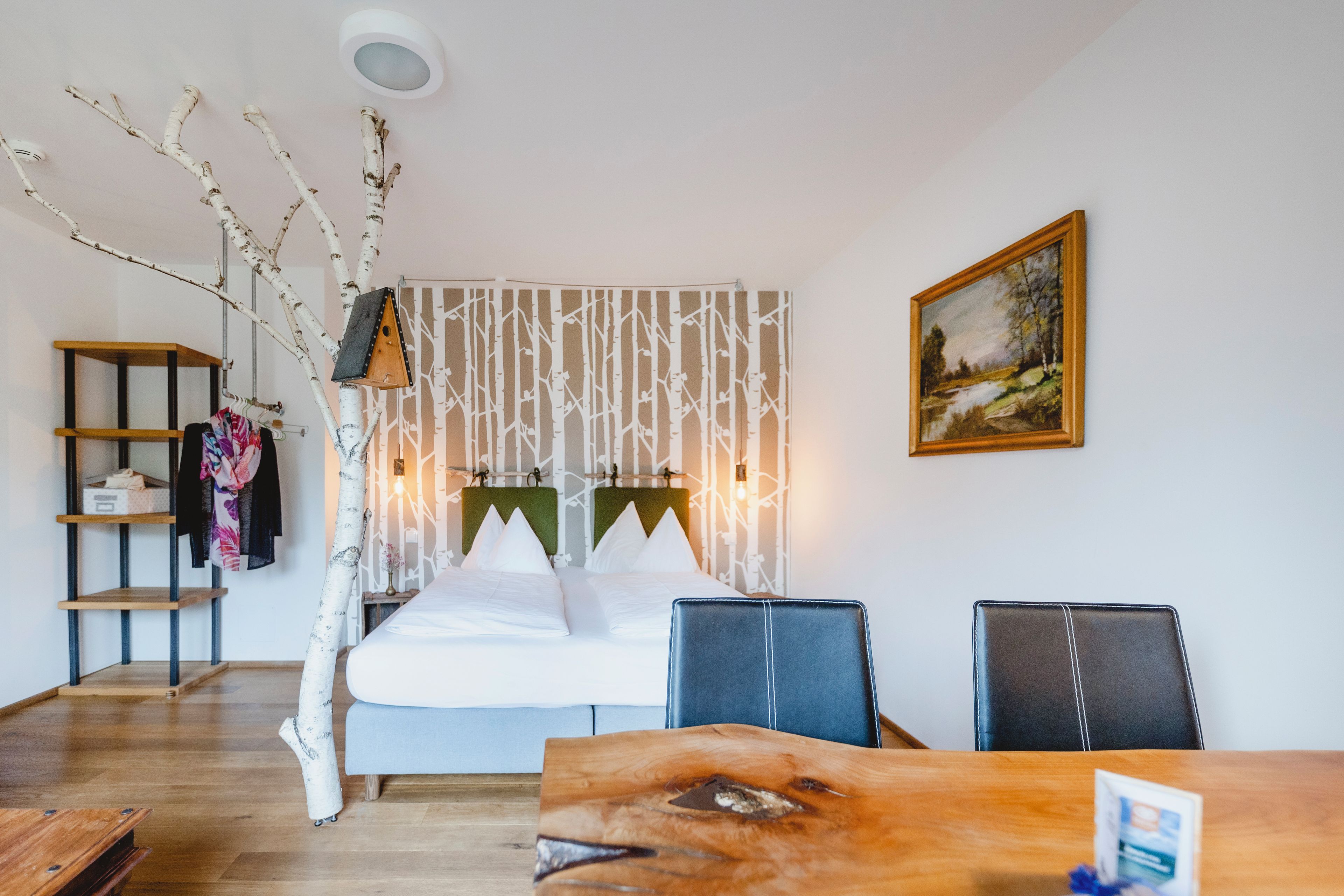 A hotel room with a bed, a desk, a chair, a wardrobe, and a painting on the wall.