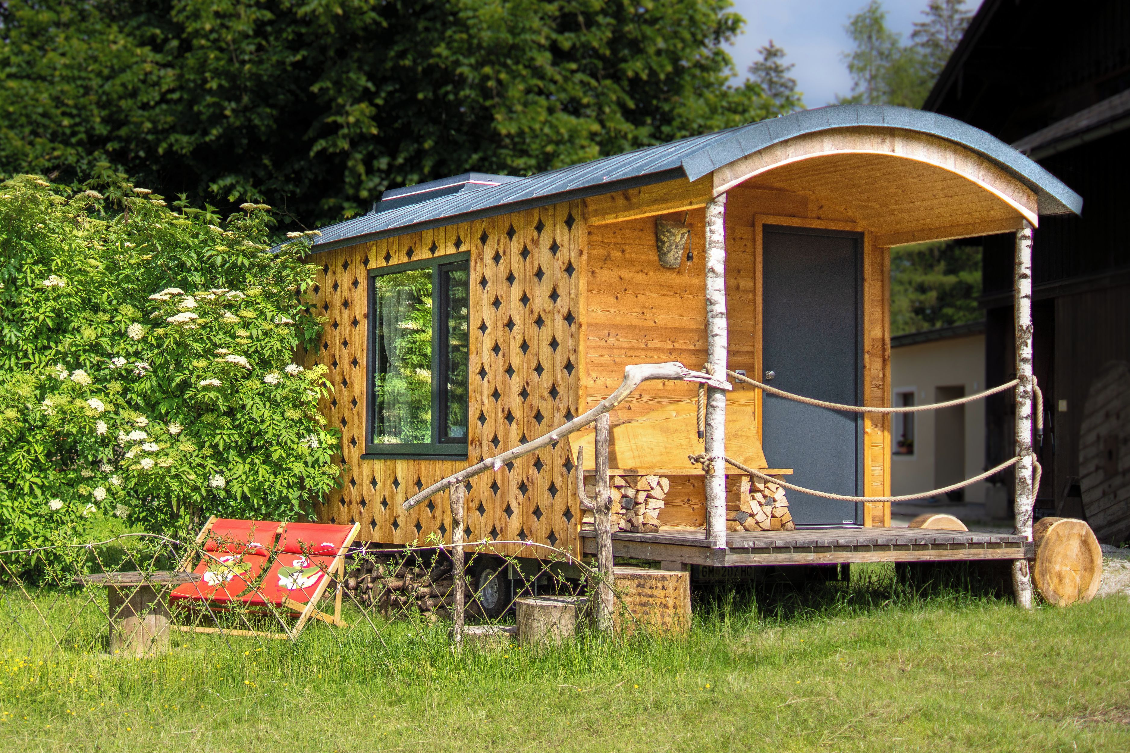 A wooden cabin with a curved roof, a small porch with a bench, and a window.