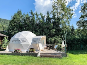 A dome-shaped structure labeled 'Clamping Dome' with a website address, surrounded by a wooden deck, outdoor seating, and a grassy area.