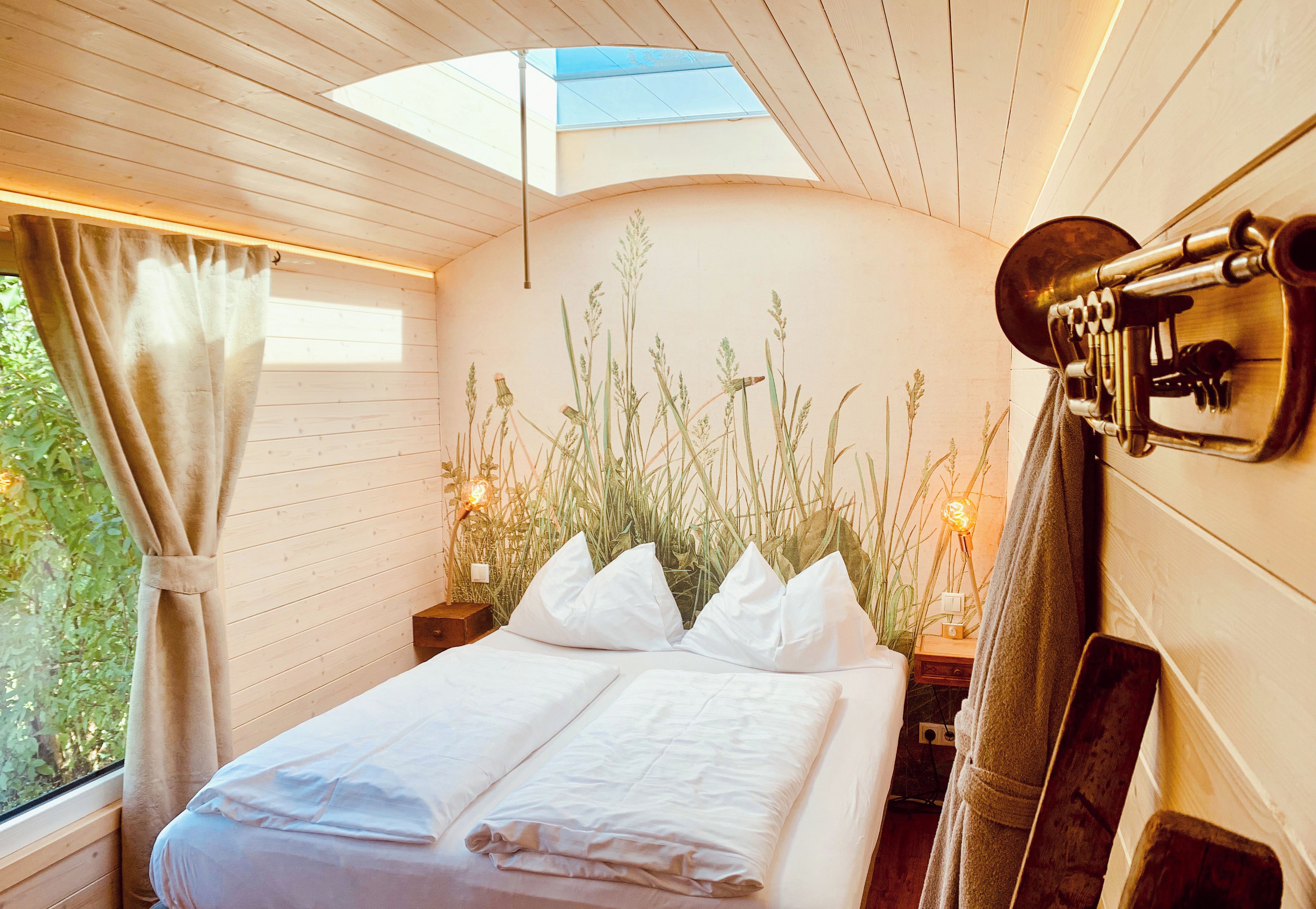 Ein Schlafzimmer mit Oberlichter, einem Bett mit weißen Leinen, einem Messing-Kopfteil und einer an der Wand befestigten Messing-Trompete.