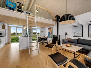 Un interior moderno con habitación tipo loft, comedor y sala de estar, con pisos de madera, una lámpara negra y obras de arte.
