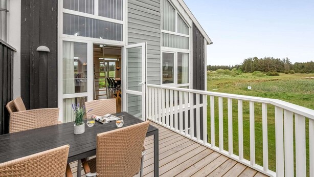 A modern house with a deck, large windows, and a view of a grassy field. - 4 Star Holiday Home in Lokken (Lokken)