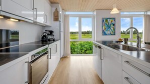 A modern kitchen with white cabinets, stainless steel appliances, and a view of greenery through large windows. - 4 Star Holiday Home in Lokken (Lokken)