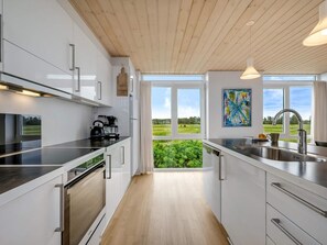 A modern kitchen with white cabinets, stainless steel appliances, and a view of greenery through large windows. - 4 Star Holiday Home in Lokken (Lokken)