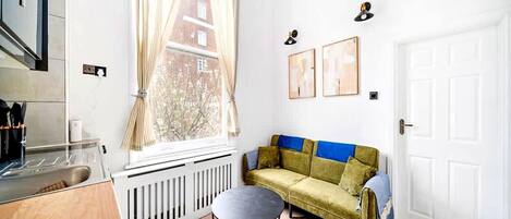 A compact living space with a kitchenette, a sofa, a round table, and a radiator.
