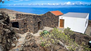 A coastal property with a stone wall, a white building with a red roof, and a view of the sea. - Holiday Home 'La Torre' with Private Terrace, Private Garden and Wi-Fi (Santa Cruz de Tenerife)