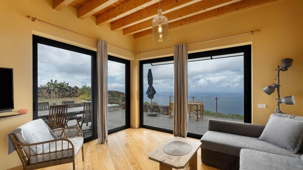 A spacious room with a wooden ceiling, large windows, a sofa, a chair, and a table. - Holiday Home 'La Torre' with Private Terrace, Private Garden and Wi-Fi (Santa Cruz de Tenerife)