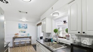 A modern kitchen with white cabinets, a stainless steel sink, a microwave, and a dining area with a bench and a small table.