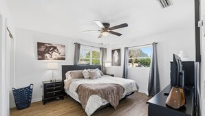 A bedroom with a bed, a ceiling fan, a TV, and a window with curtains.