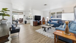 A modern living room with a TV, sofa, coffee table, and a dining area with chairs and a table.