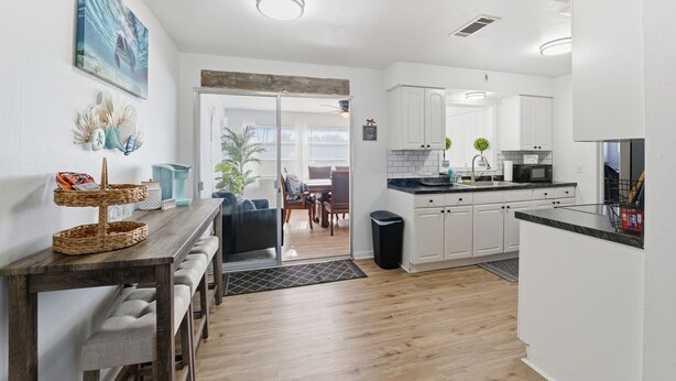 A modern kitchen with white cabinets, a black countertop, and a dining area with a wooden table and benches.