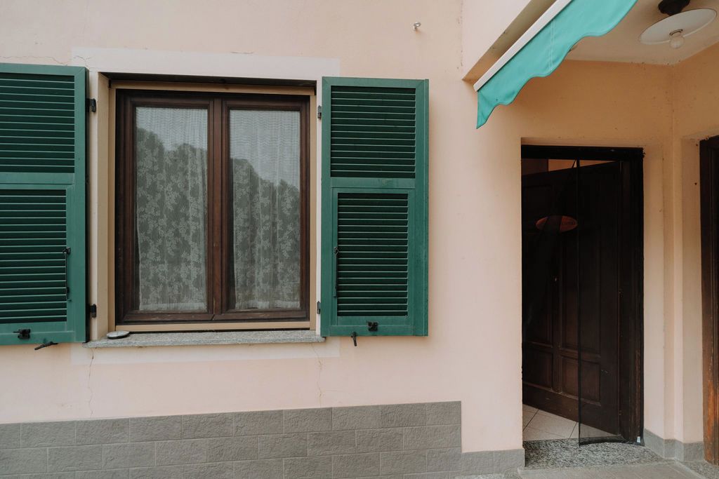 A building with a window with green shutters, a door, and a small balcony.