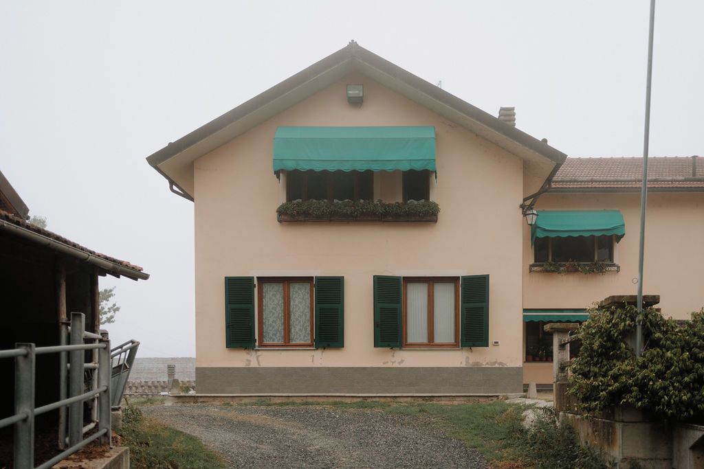 Un edificio a due piani con tetto spiovente, tende verdi sopra le finestre e vialetto in ghiaia.