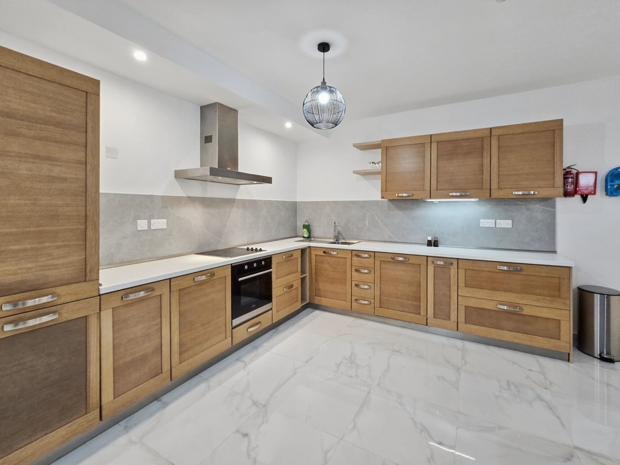 Une cuisine moderne avec des meubles en bois, une hotte en acier inoxydable, un plan de travail en marbre et un luminaire suspendu.