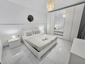 A modern bedroom with a large bed, bedside tables, a mirror, and a hanging light fixture. - Close to Promenade 2 bedroom modern apartment with nice yard, Family Friendly (San Pawl il-Baħar)