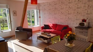 Una sala moderna con un sofá rojo, un sillón gris, una mesa de centro de madera y una mesa de comedor con mantel estampado.