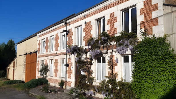 Un edificio de ladrillo de dos pisos con marcos de ventana blancos, un sendero de piedra y enredaderas moradas en flor.