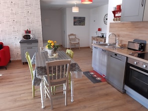 A modern kitchen with a dining area, wooden flooring, and a red chair.